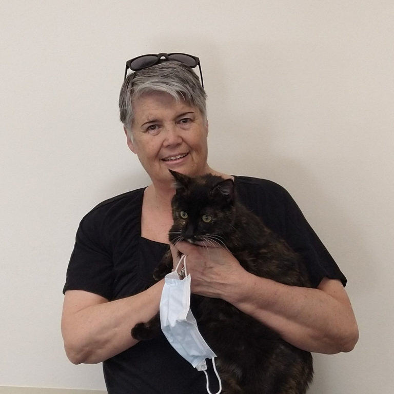 An older woman with short, gray hair holds a black and brown cat