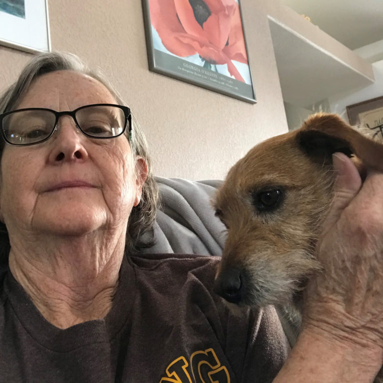 An older woman takes a selfie of her and a small, brown dog