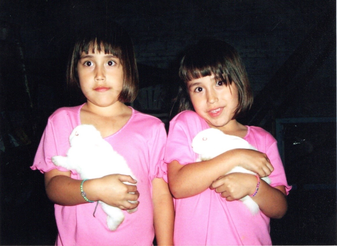 Two girl twins in pink shirts holding white bunnies