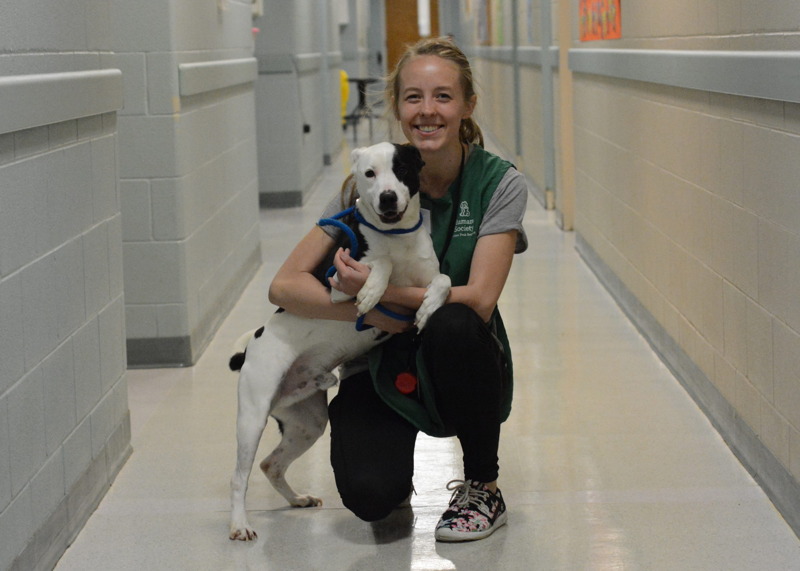 A young, blonde woman smiling with a black and white dog